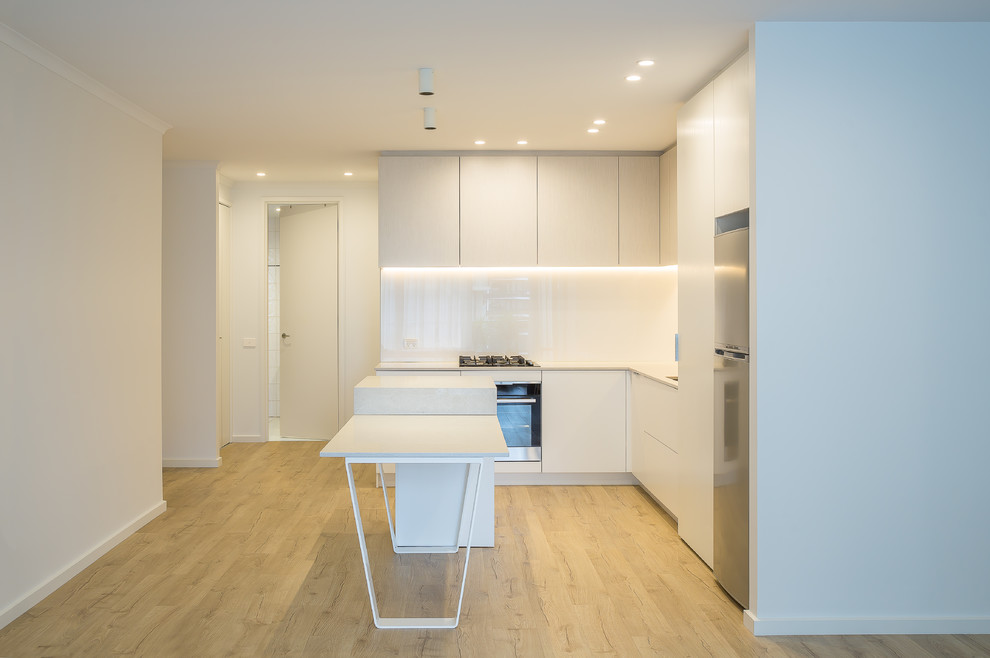 Photo of a mid-sized modern l-shaped open plan kitchen in Melbourne with an undermount sink, open cabinets, white cabinets, quartz benchtops, white splashback, glass sheet splashback, black appliances, laminate floors, with island, beige floor and grey benchtop.