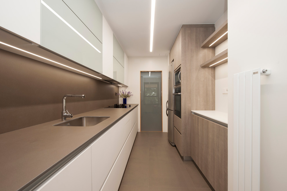 Design ideas for a mid-sized modern galley separate kitchen in Barcelona with a single-bowl sink, flat-panel cabinets, white cabinets, limestone benchtops, brown splashback, limestone splashback, black appliances, porcelain floors, no island and brown floor.