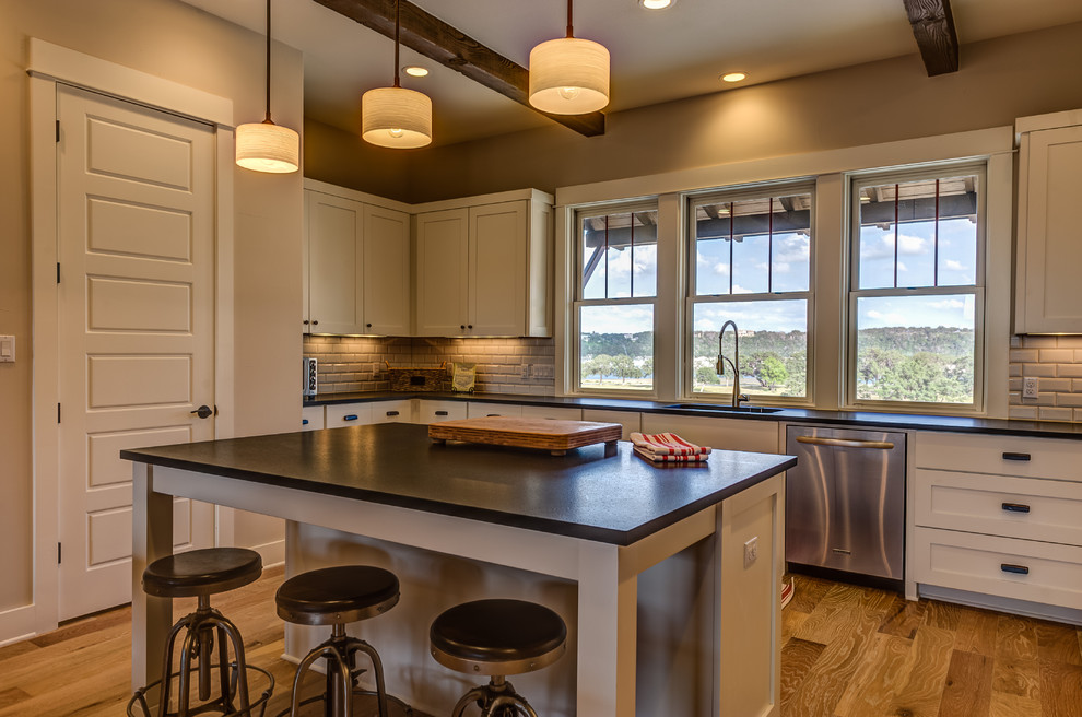 Photo of a large country l-shaped eat-in kitchen in Austin with an undermount sink, shaker cabinets, white cabinets, grey splashback, subway tile splashback, stainless steel appliances, light hardwood floors and with island.