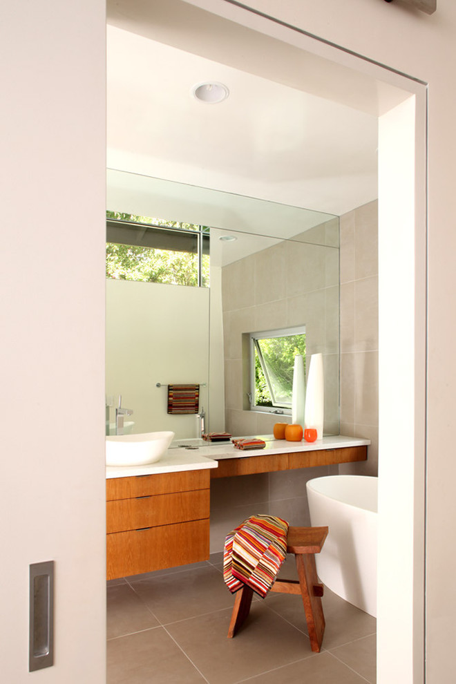 Mid-sized modern master bathroom in Los Angeles with flat-panel cabinets, medium wood cabinets, a freestanding tub, beige tile, stone tile, beige walls, porcelain floors, a vessel sink, engineered quartz benchtops and beige floor.