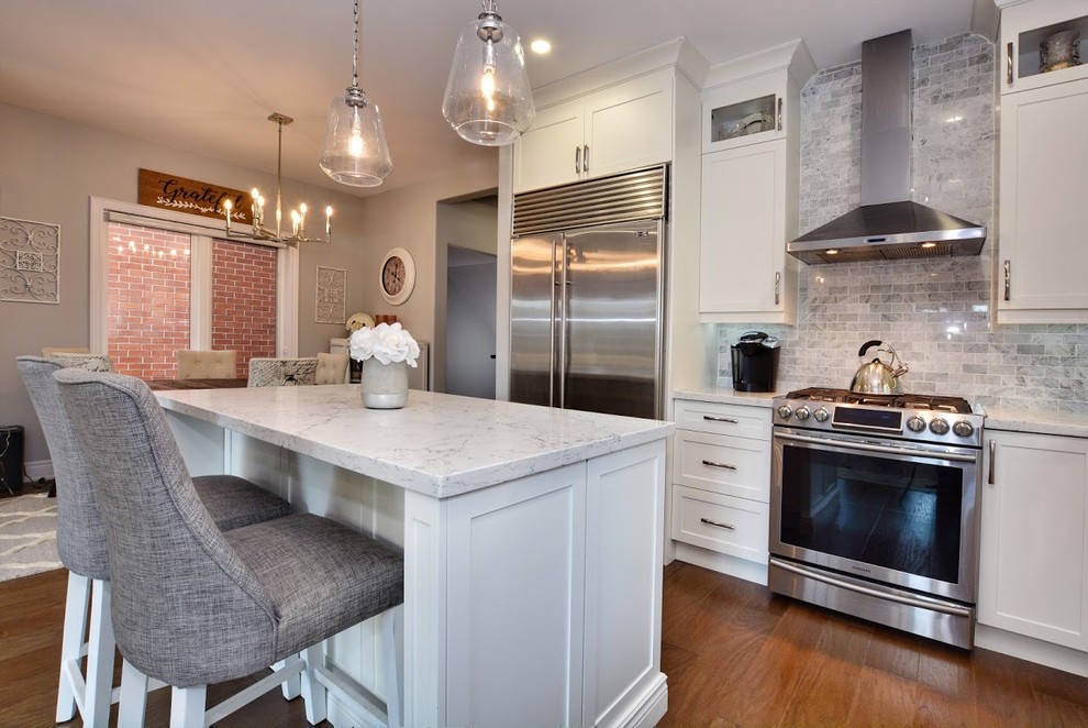 Inspiration for a mid-sized transitional l-shaped medium tone wood floor and brown floor eat-in kitchen remodel in Toronto with a farmhouse sink, shaker cabinets, white cabinets, quartz countertops, gray backsplash, marble backsplash, stainless steel appliances, an island and white countertops