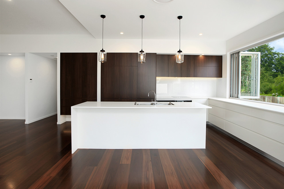 Photo of a mid-sized modern l-shaped open plan kitchen in Sunshine Coast with an undermount sink, stainless steel appliances, with island, flat-panel cabinets, dark wood cabinets, granite benchtops, white splashback and glass sheet splashback.