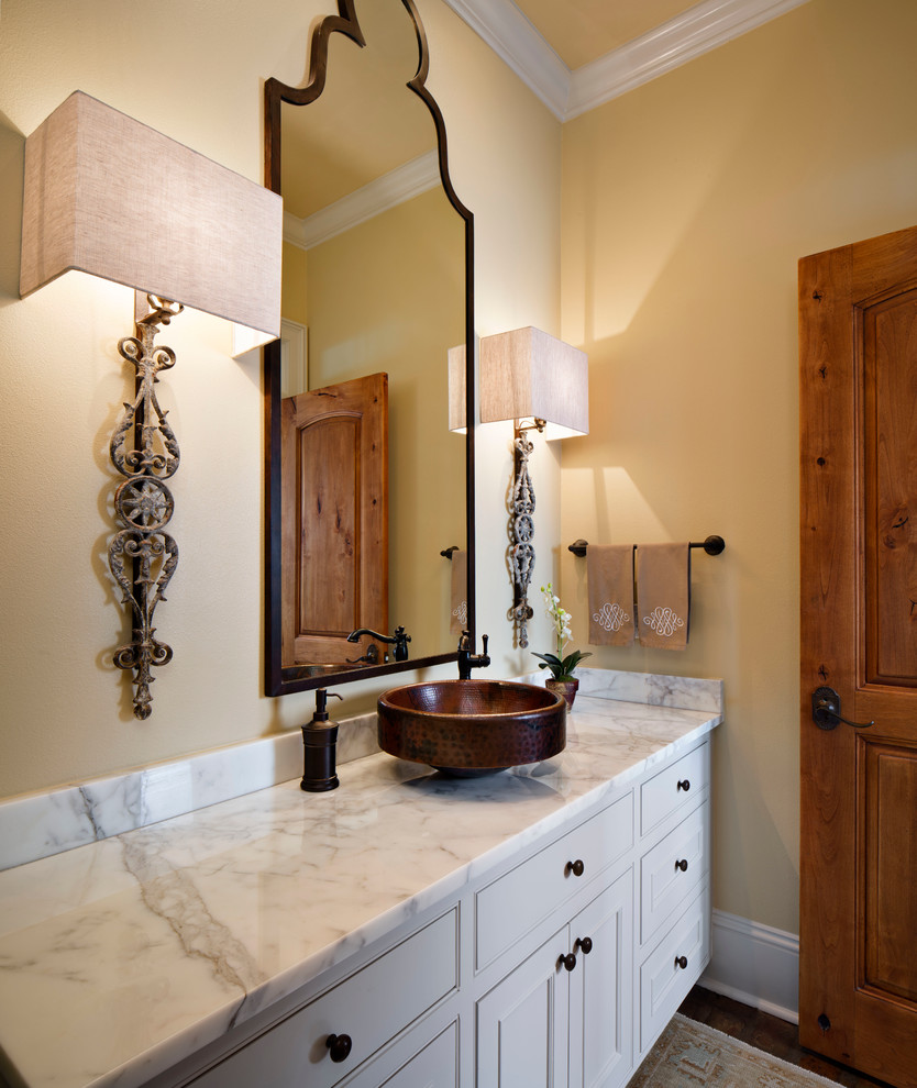 This is an example of a mid-sized traditional powder room in New Orleans with a vessel sink, beaded inset cabinets, white cabinets, marble benchtops, yellow walls and white benchtops.