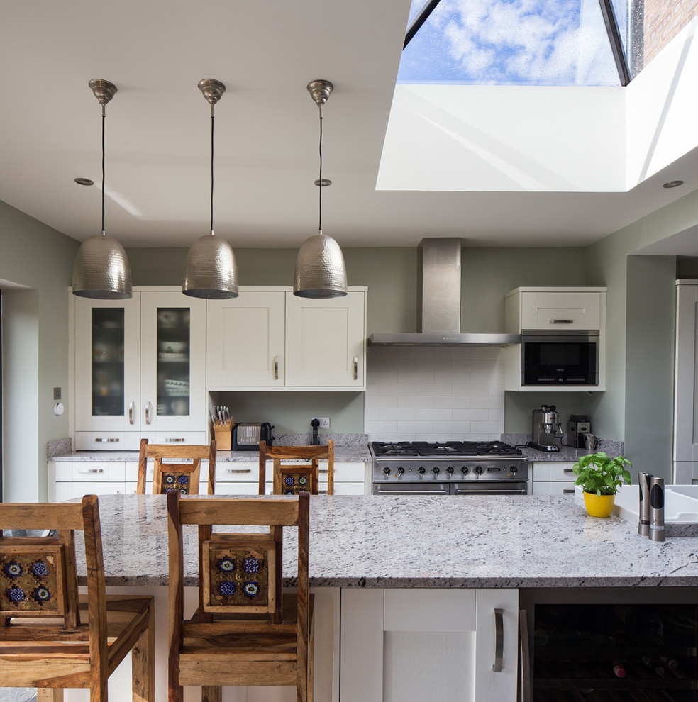 This is an example of a large transitional u-shaped open plan kitchen in Hertfordshire with a farmhouse sink, shaker cabinets, white cabinets, marble benchtops, white splashback, ceramic splashback, stainless steel appliances, slate floors and a peninsula.