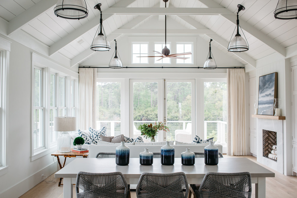 Inspiration for a mid-sized beach style dining room in Charleston with white walls, light hardwood floors, a standard fireplace, a stone fireplace surround and beige floor.