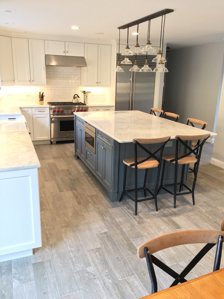 This is an example of a large country l-shaped eat-in kitchen in New York with a farmhouse sink, recessed-panel cabinets, white cabinets, quartzite benchtops, white splashback, ceramic splashback, stainless steel appliances, porcelain floors and with island.