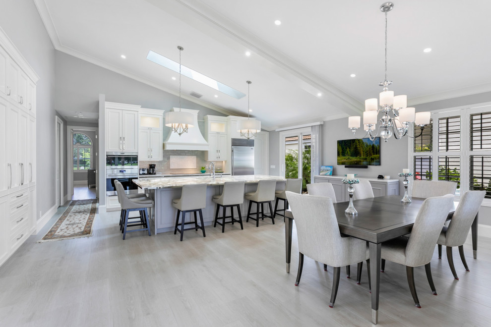 Expansive transitional single-wall eat-in kitchen in Miami with a drop-in sink, raised-panel cabinets, white cabinets, quartzite benchtops, glass tile splashback, stainless steel appliances, porcelain floors, with island, grey floor, multi-coloured benchtop, vaulted and green splashback.