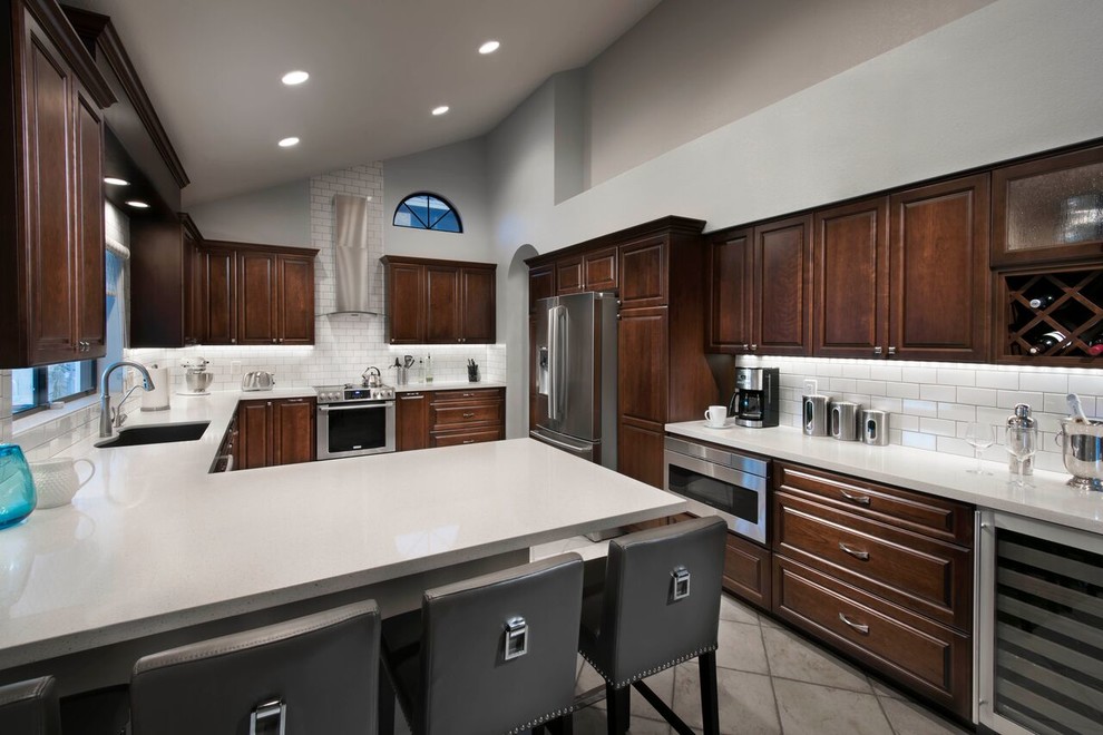 Example of a large transitional u-shaped ceramic tile eat-in kitchen design in Phoenix with an undermount sink, raised-panel cabinets, dark wood cabinets, quartz countertops, white backsplash, subway tile backsplash, stainless steel appliances and a peninsula