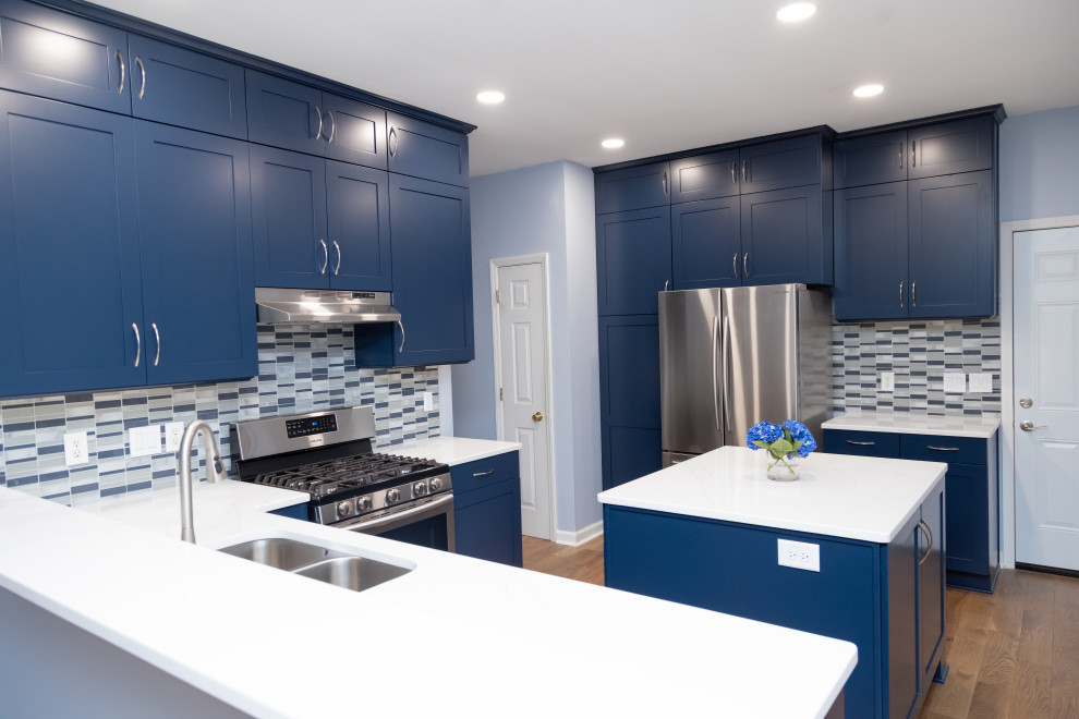 Große Moderne Wohnküche in U-Form mit Schrankfronten im Shaker-Stil, blauen Schränken, Quarzwerkstein-Arbeitsplatte, Rückwand aus Glasfliesen, Kücheninsel und weißer Arbeitsplatte in Sonstige