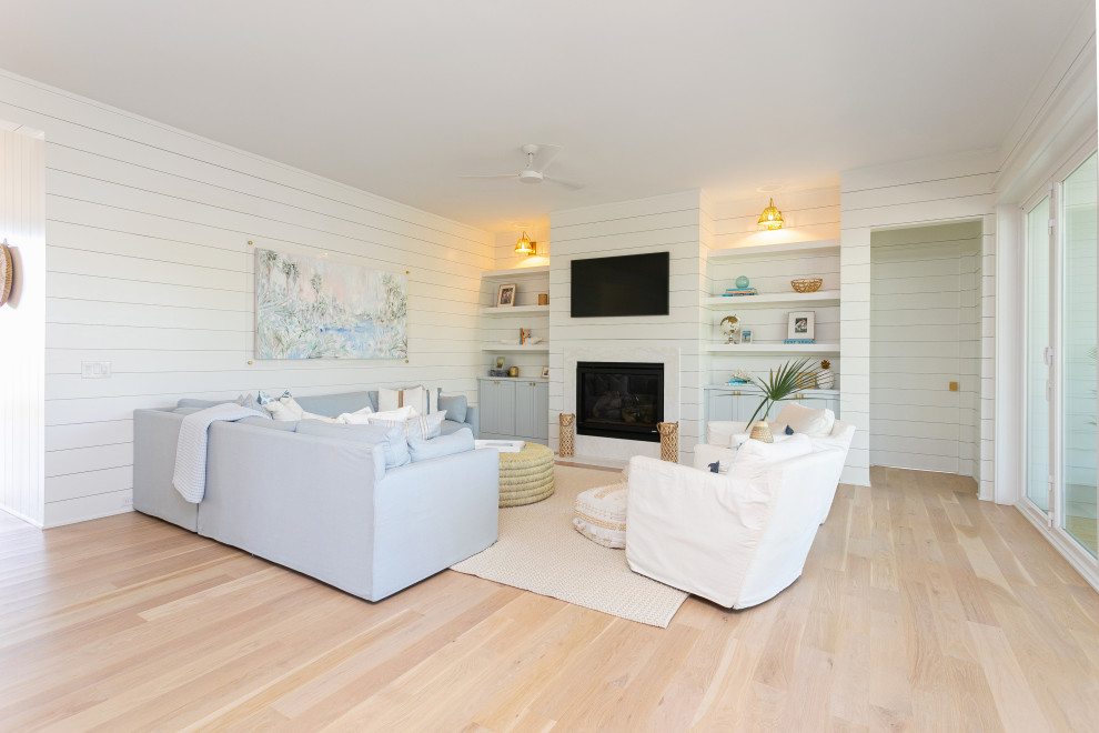 Großes, Offenes Maritimes Wohnzimmer mit weißer Wandfarbe, hellem Holzboden, Kamin, Kaminumrandung aus Stein, TV-Wand und Holzdielenwänden in Charleston