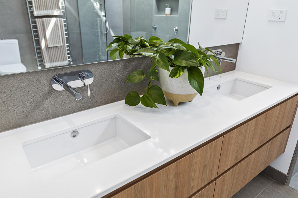 This is an example of a mid-sized contemporary master bathroom in Geelong with flat-panel cabinets, light wood cabinets, porcelain floors, a drop-in sink, solid surface benchtops and grey floor.