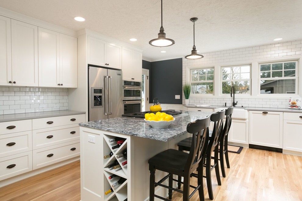 Mid-sized country u-shaped eat-in kitchen in Portland with a farmhouse sink, flat-panel cabinets, white cabinets, quartzite benchtops, white splashback, subway tile splashback, stainless steel appliances, medium hardwood floors and with island.