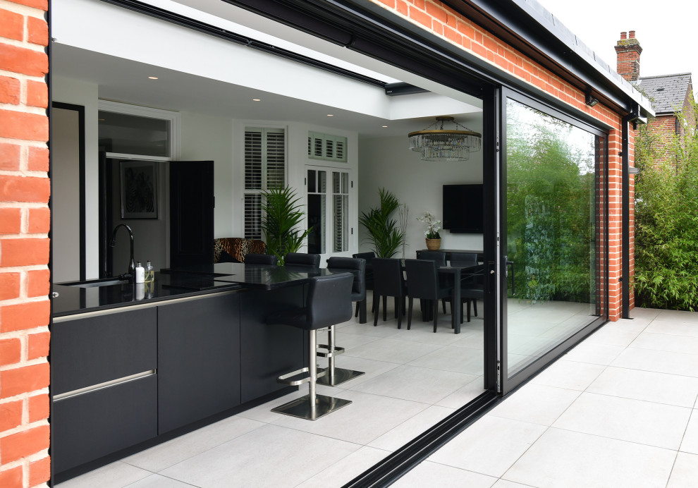 This is an example of a medium sized modern kitchen/diner in Essex with flat-panel cabinets, black splashback, ceramic flooring, an island, beige floors and black worktops.