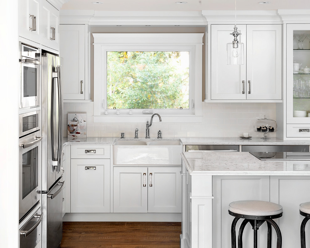 Design ideas for a mid-sized traditional l-shaped eat-in kitchen in Vancouver with a farmhouse sink, shaker cabinets, white cabinets, quartz benchtops, white splashback, subway tile splashback, stainless steel appliances, light hardwood floors, with island and brown floor.