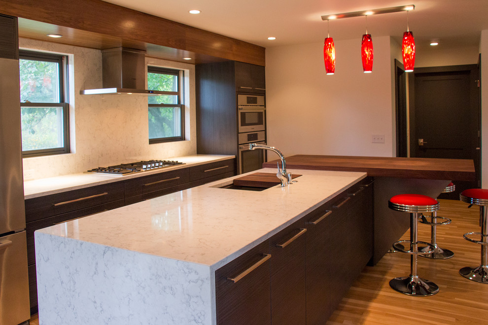 Design ideas for a mid-sized contemporary single-wall eat-in kitchen in Milwaukee with an undermount sink, flat-panel cabinets, dark wood cabinets, quartz benchtops, grey splashback, stone slab splashback, stainless steel appliances, light hardwood floors and with island.