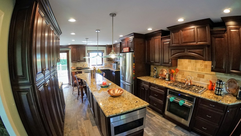 Large transitional l-shaped ceramic tile and brown floor eat-in kitchen photo in New York with an undermount sink, raised-panel cabinets, brown cabinets, granite countertops, beige backsplash, marble backsplash, stainless steel appliances and an island