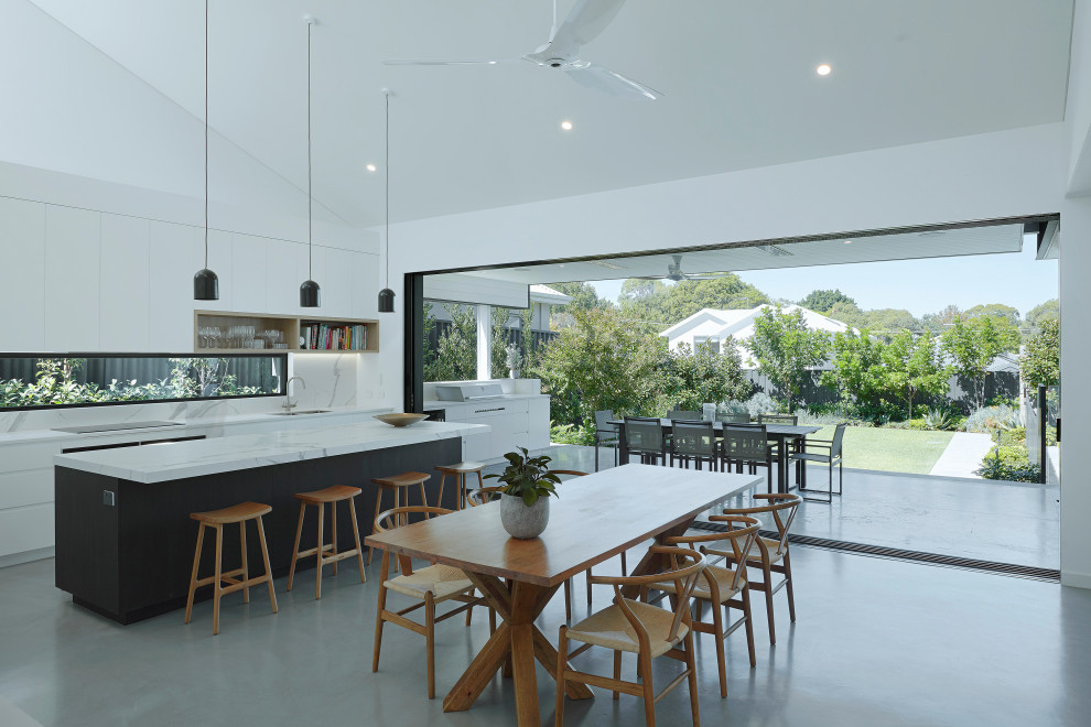Minimalist galley concrete floor, gray floor and vaulted ceiling eat-in kitchen photo in Perth with an undermount sink, flat-panel cabinets, white cabinets, white backsplash, window backsplash, an island, white countertops, quartz countertops and stainless steel appliances
