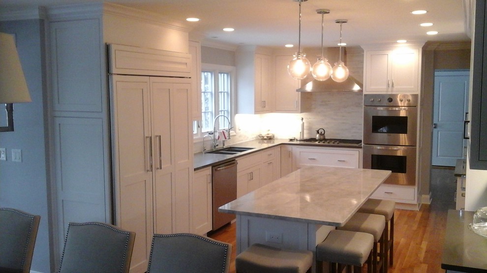 Inspiration for a mid-sized transitional l-shaped light wood floor eat-in kitchen remodel in Newark with a double-bowl sink, shaker cabinets, white cabinets, solid surface countertops, multicolored backsplash, stone tile backsplash, stainless steel appliances and an island