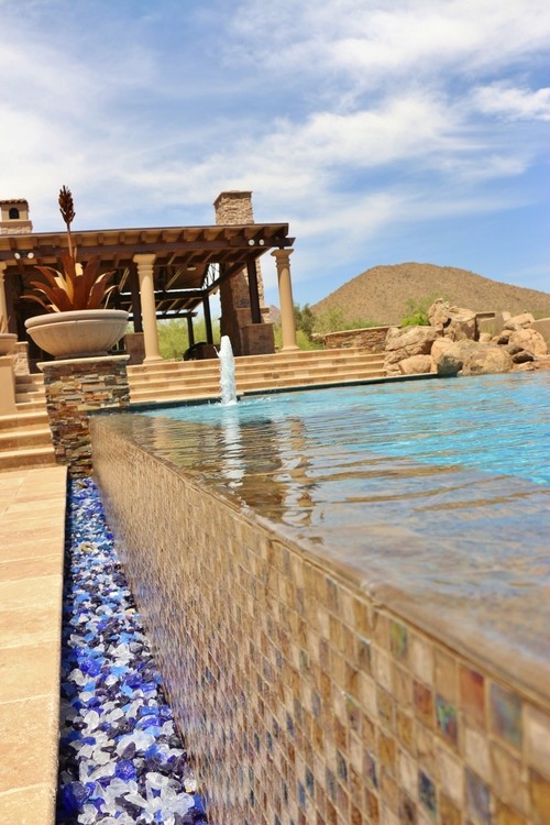 Large backyard concrete paver and custom-shaped infinity pool fountain photo in Phoenix