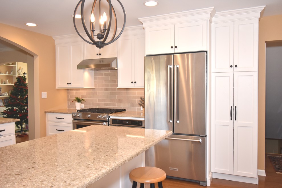 Photo of a small traditional u-shaped eat-in kitchen in Chicago with an integrated sink, shaker cabinets, white cabinets, quartz benchtops, beige splashback, porcelain splashback, stainless steel appliances, medium hardwood floors, a peninsula, brown floor and beige benchtop.