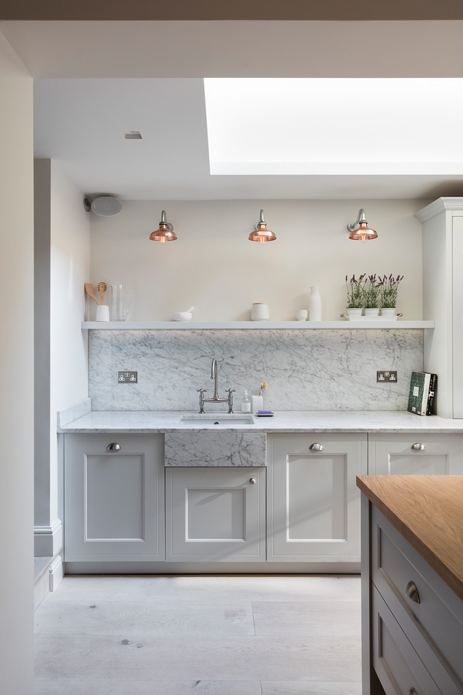 Design ideas for a small transitional single-wall kitchen in London with a farmhouse sink, shaker cabinets, grey cabinets, marble benchtops, grey splashback, marble splashback, panelled appliances, light hardwood floors, with island and white floor.