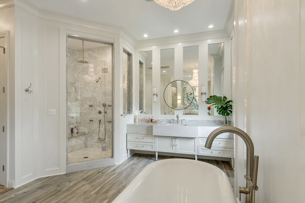 Design ideas for a transitional bathroom in New Orleans with shaker cabinets, white cabinets, a freestanding tub, white tile, white walls, medium hardwood floors and a hinged shower door.