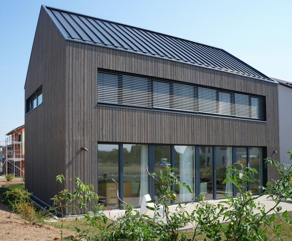 This is an example of a modern two floor detached house in Frankfurt with wood cladding, a pitched roof, a metal roof, a black roof and shiplap cladding.