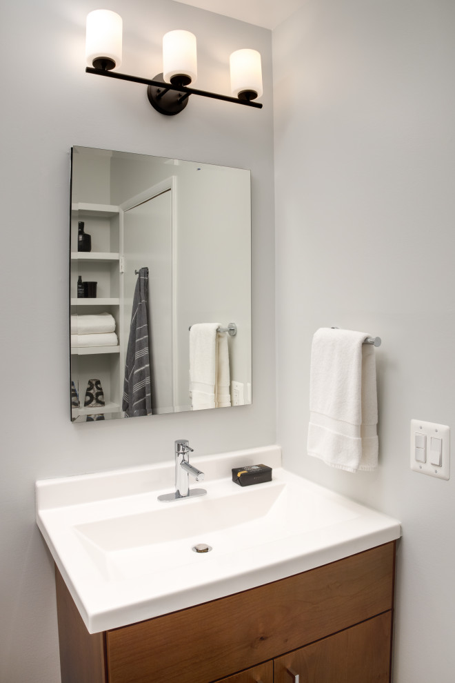 Пример оригинального дизайна: маленькая ванная комната в стиле модернизм с плоскими фасадами, фасадами цвета дерева среднего тона, душем в нише, раздельным унитазом, белой плиткой, керамической плиткой, серыми стенами, полом из керамической плитки, душевой кабиной, монолитной раковиной, столешницей из искусственного камня, черным полом, душем с распашными дверями, белой столешницей, нишей, тумбой под одну раковину и встроенной тумбой для на участке и в саду