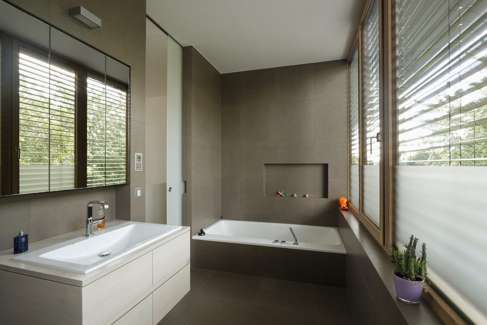 Photo of a large contemporary bathroom in Frankfurt with flat-panel cabinets, light wood cabinets, an alcove tub, brown tile, brown walls, a drop-in sink and wood benchtops.