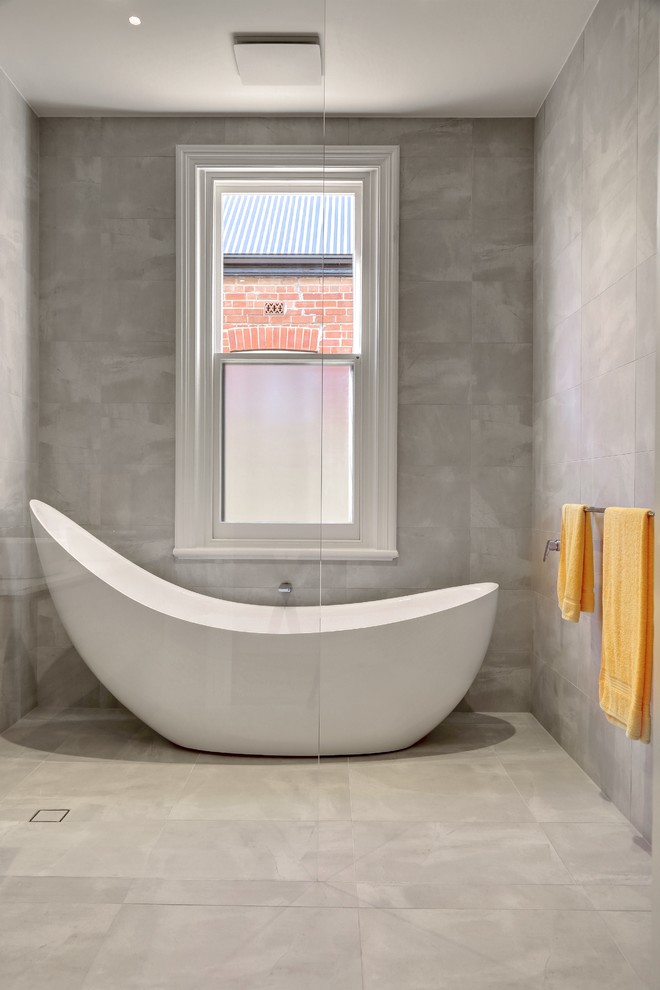 Design ideas for a mid-sized contemporary master wet room bathroom in Adelaide with furniture-like cabinets, light wood cabinets, a freestanding tub, a wall-mount toilet, gray tile, ceramic tile, ceramic floors, a console sink, engineered quartz benchtops, grey floor, an open shower and white benchtops.