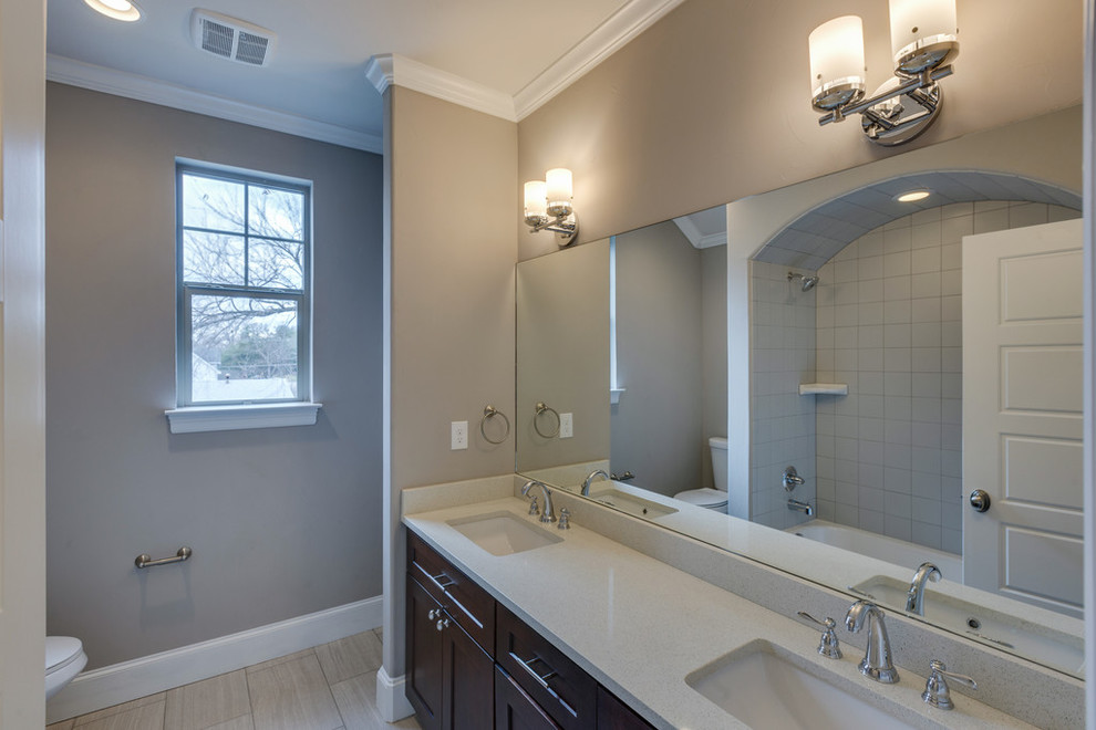 This is an example of a large transitional 3/4 bathroom in Dallas with a drop-in tub, a shower/bathtub combo, a one-piece toilet, gray tile, ceramic tile, grey walls, ceramic floors, a drop-in sink, recessed-panel cabinets, brown cabinets and quartzite benchtops.