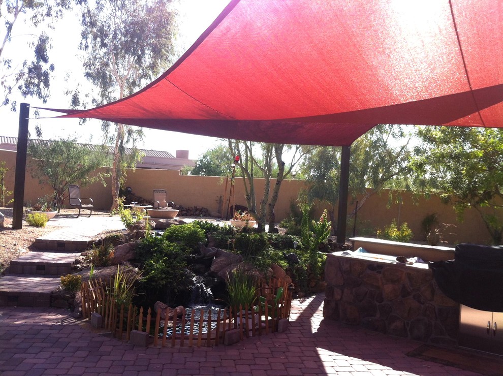 This is an example of a large country backyard patio in Phoenix with an outdoor kitchen, brick pavers and an awning.