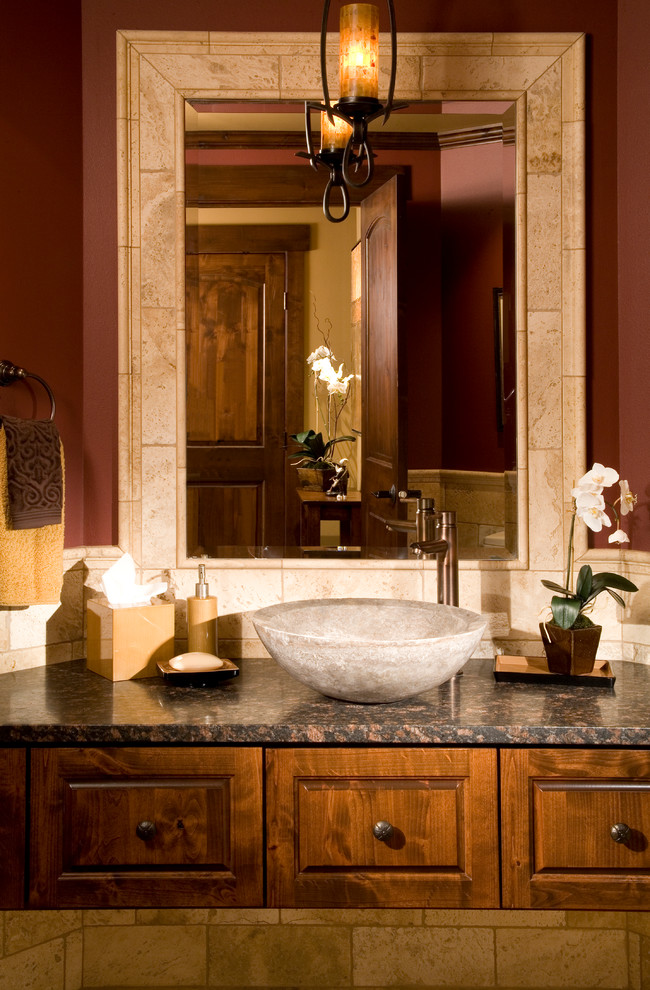 Inspiration for a mid-sized transitional powder room in Denver with a vessel sink, medium wood cabinets, marble benchtops, beige tile, red walls, travertine and raised-panel cabinets.