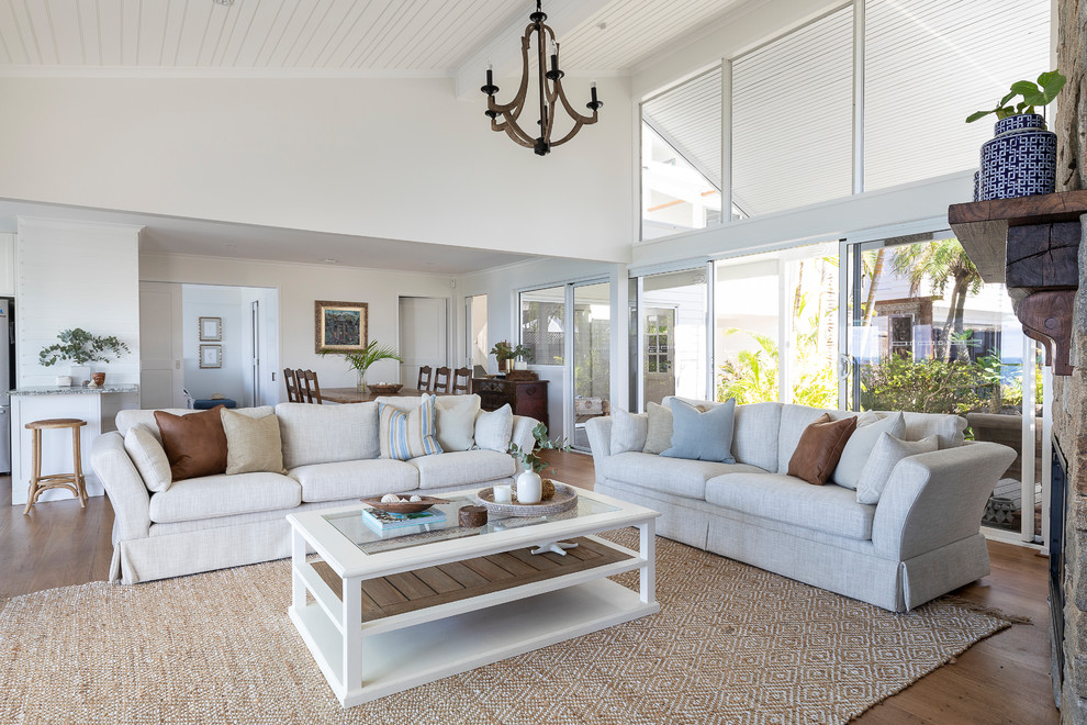 This is an example of a large tropical formal open concept living room in Sunshine Coast with white walls, medium hardwood floors, a standard fireplace, a stone fireplace surround and a freestanding tv.