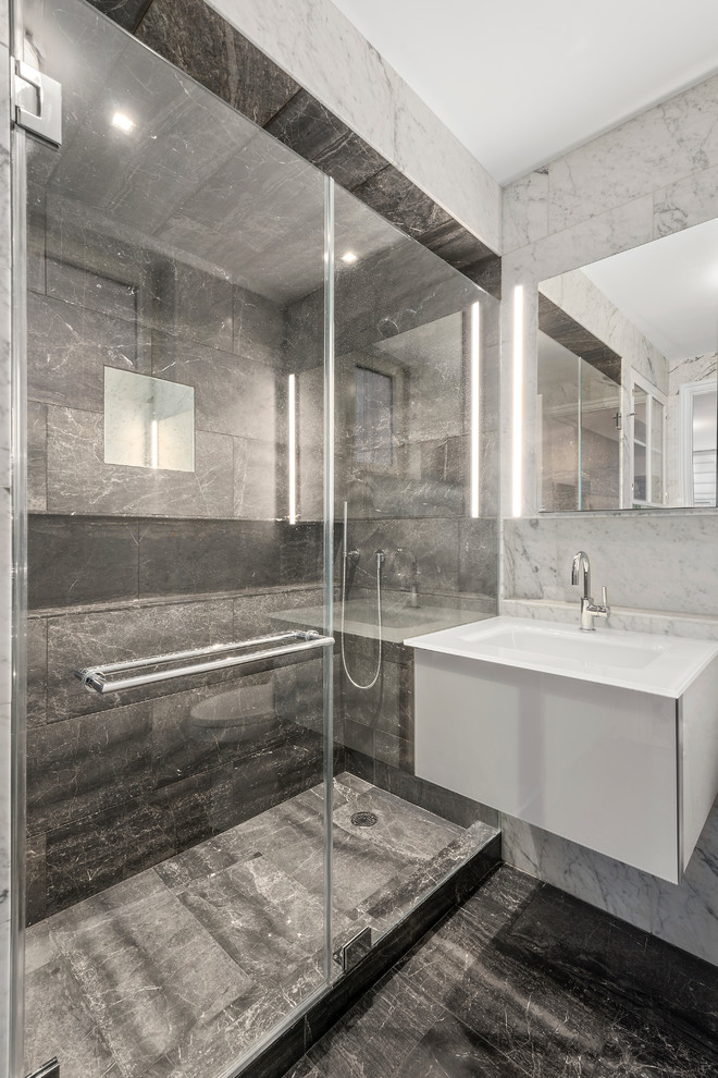 This is an example of a small modern master bathroom in New York with an alcove shower, a one-piece toilet, black walls, marble floors, a wall-mount sink and a hinged shower door.