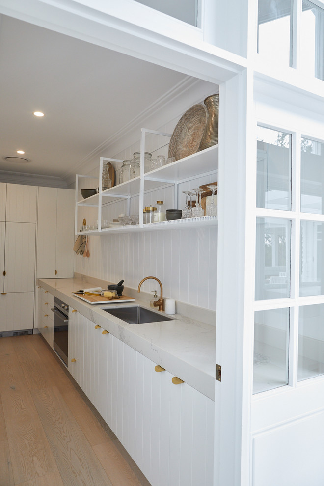 Photo of a large beach style l-shaped kitchen pantry in Sydney with an undermount sink, white cabinets, white splashback, panelled appliances, no island and white benchtop.