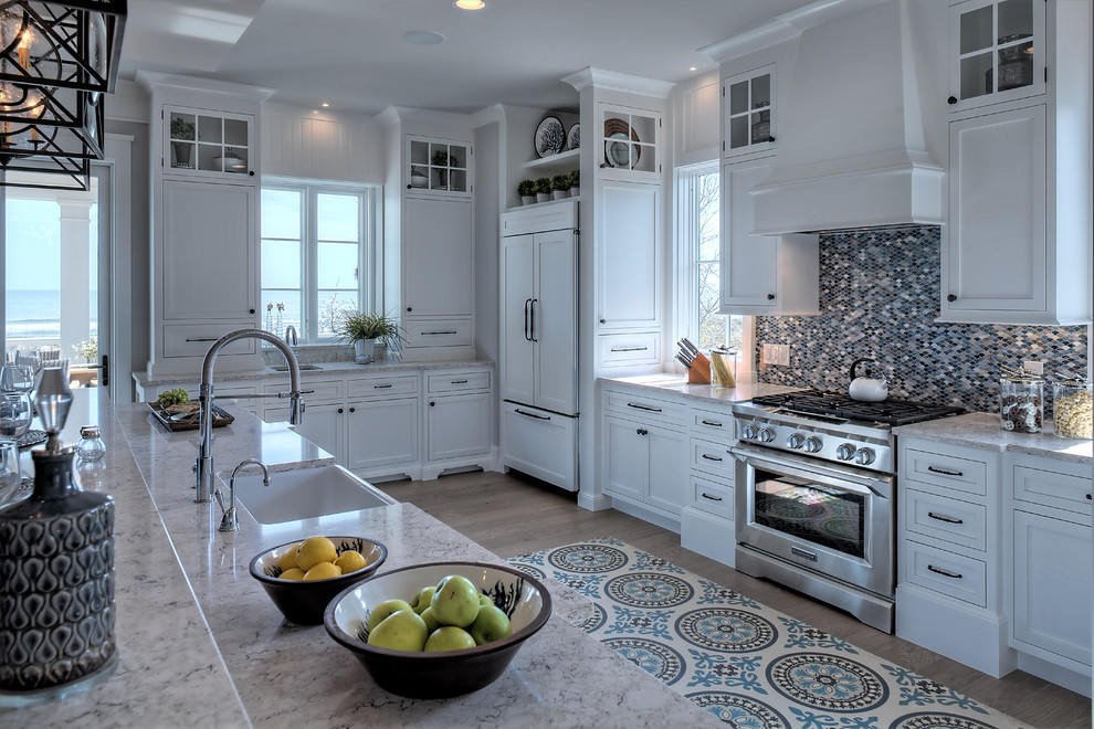 Inspiration for a beach style kitchen in Other with a farmhouse sink, shaker cabinets, white cabinets, multi-coloured splashback, mosaic tile splashback, stainless steel appliances, medium hardwood floors, with island, brown floor and grey benchtop.