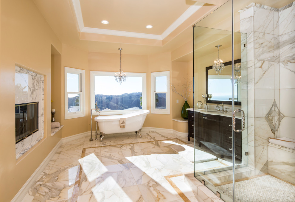 Inspiration for an expansive mediterranean master bathroom in Los Angeles with recessed-panel cabinets, dark wood cabinets, a claw-foot tub, a corner shower, a one-piece toilet, white tile, stone tile, beige walls, marble floors, marble benchtops, an undermount sink, grey floor and a hinged shower door.