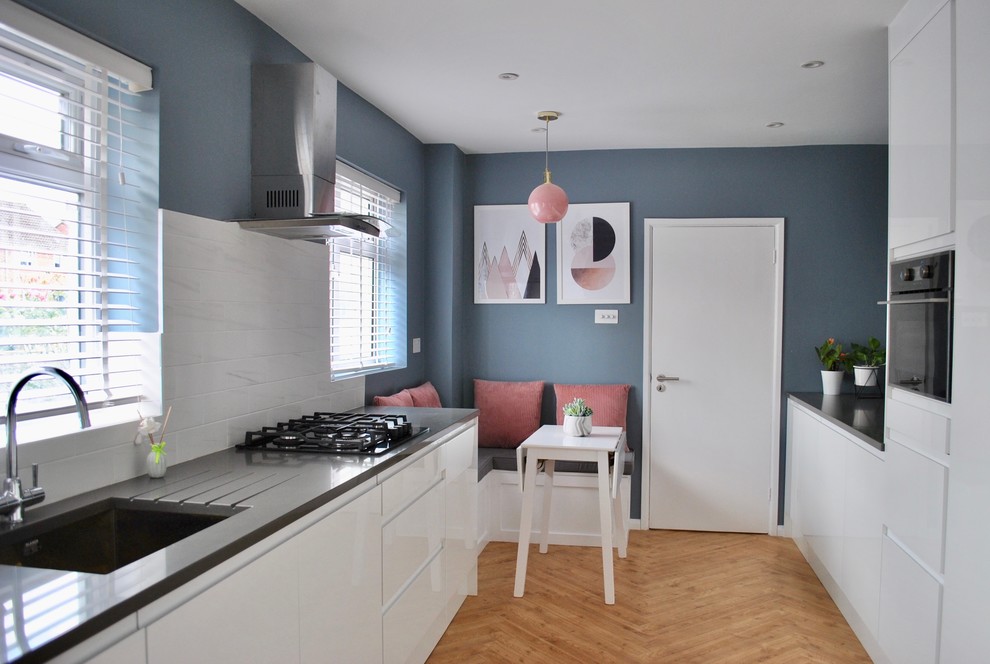 Mid-sized modern galley eat-in kitchen in Hertfordshire with a drop-in sink, flat-panel cabinets, white cabinets, white splashback, porcelain splashback, panelled appliances and grey benchtop.