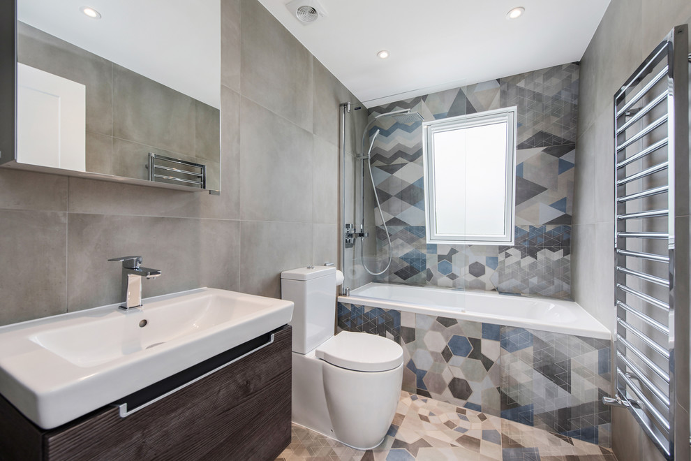 Photo of a large contemporary kids bathroom in London with dark wood cabinets, a drop-in tub, a shower/bathtub combo, flat-panel cabinets, multi-coloured tile, an integrated sink, an open shower, a one-piece toilet, cement tile, multi-coloured walls and cement tiles.