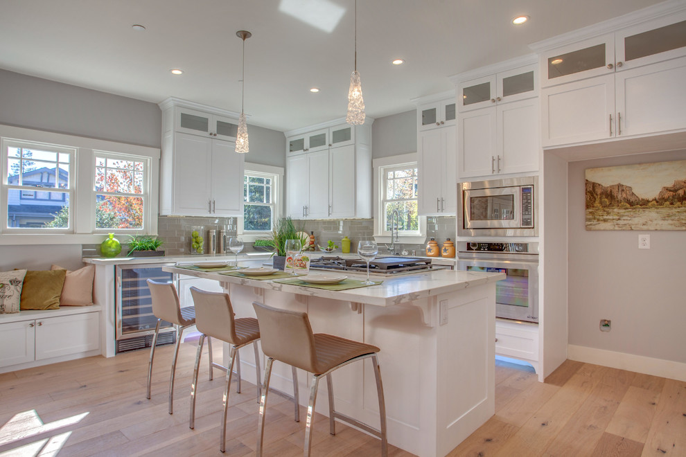 Photo of a country kitchen in San Francisco with shaker cabinets, white cabinets, marble benchtops, grey splashback, ceramic splashback, stainless steel appliances, light hardwood floors and with island.