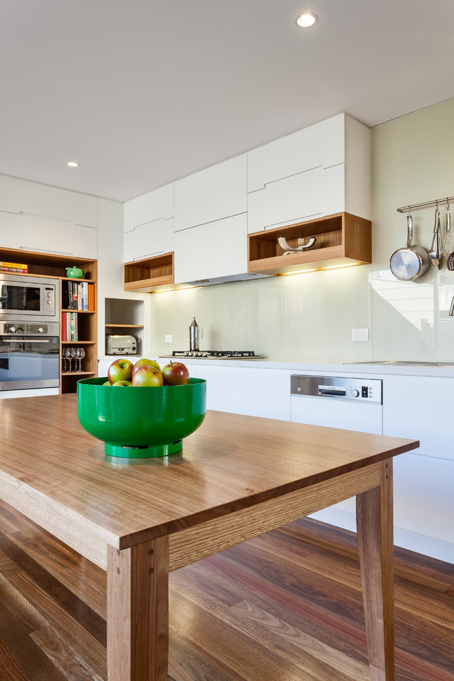 Design ideas for a contemporary l-shaped eat-in kitchen in Sydney with a drop-in sink, flat-panel cabinets, white cabinets, quartz benchtops, white splashback, glass sheet splashback, stainless steel appliances and medium hardwood floors.