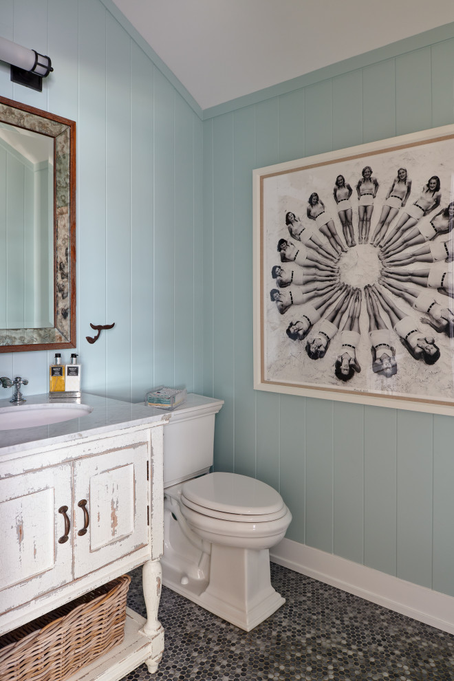 This is an example of a beach style powder room in New York with furniture-like cabinets, distressed cabinets, blue walls, mosaic tile floors, an undermount sink, black floor and white benchtops.