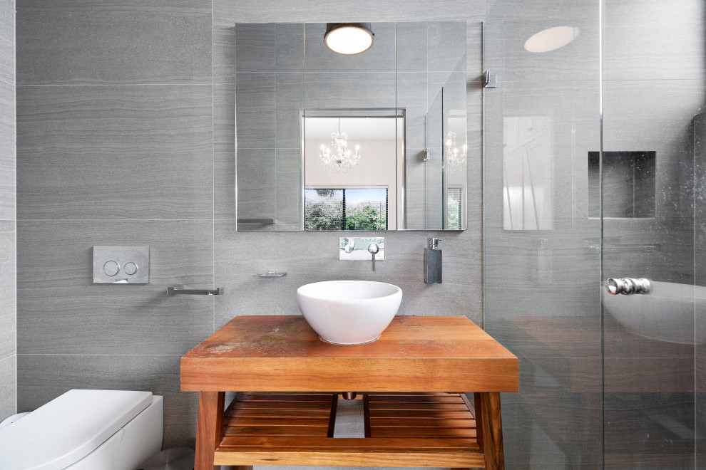 Photo of a small contemporary 3/4 bathroom in Sydney with medium wood cabinets, a corner shower, a wall-mount toilet, gray tile, cement tile, grey walls, cement tiles, a vessel sink, wood benchtops, grey floor, a hinged shower door, a niche, a single vanity and a freestanding vanity.