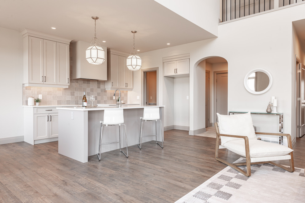 Small transitional galley laminate floor and brown floor open concept kitchen photo in Toronto with a double-bowl sink, recessed-panel cabinets, beige cabinets, quartz countertops, beige backsplash, porcelain backsplash, stainless steel appliances, an island and white countertops