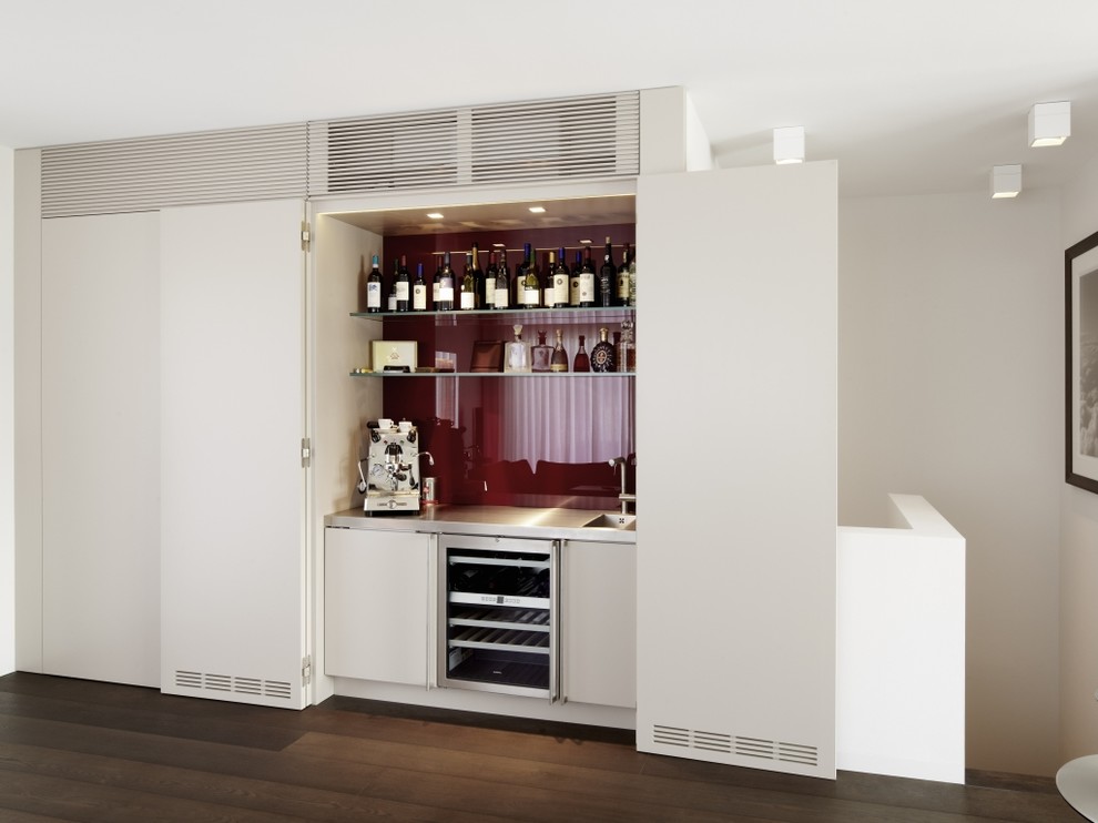 Photo of a mid-sized contemporary single-wall home bar in Frankfurt with an integrated sink, flat-panel cabinets, white cabinets, red splashback and dark hardwood floors.
