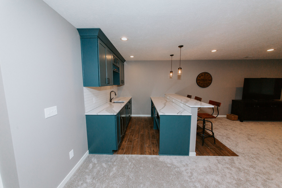 Photo of a small transitional galley seated home bar in Omaha with an undermount sink, shaker cabinets, green cabinets, marble benchtops, white splashback, subway tile splashback, medium hardwood floors and brown floor.