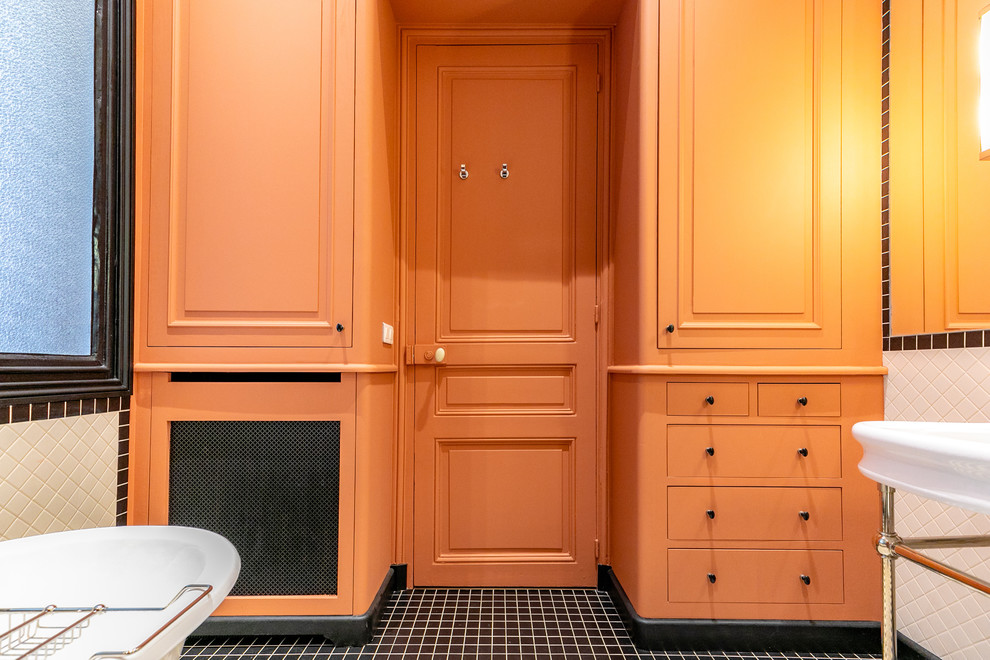 Photo of a mid-sized transitional master bathroom in Grenoble with beaded inset cabinets, orange cabinets, a claw-foot tub, an alcove shower, white tile, subway tile, orange walls, cement tiles, a console sink, solid surface benchtops, black floor, a hinged shower door and white benchtops.
