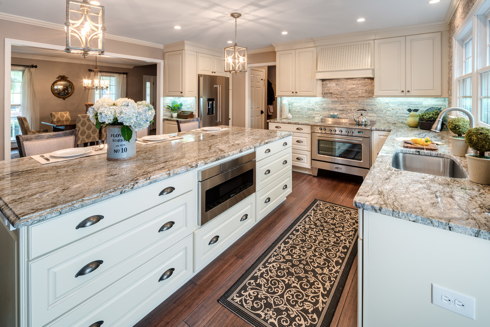 Large traditional u-shaped eat-in kitchen in Atlanta with an undermount sink, raised-panel cabinets, white cabinets, granite benchtops, stainless steel appliances, bamboo floors, with island, brown floor, brown splashback, stone tile splashback and multi-coloured benchtop.