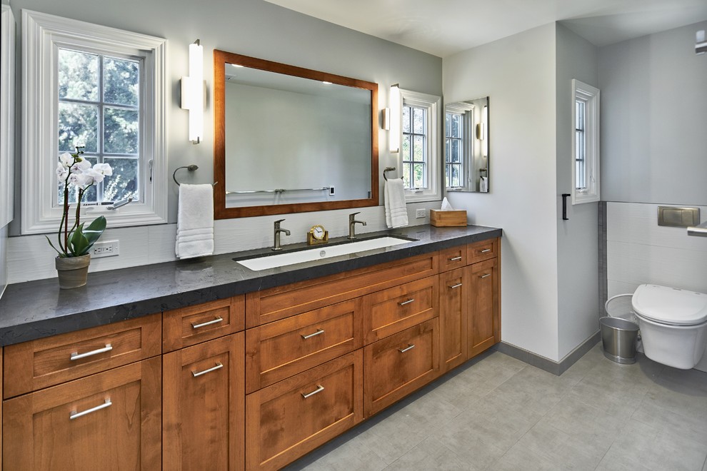 Mid-sized transitional kids bathroom in San Francisco with shaker cabinets, medium wood cabinets, a corner tub, a shower/bathtub combo, a one-piece toilet, white tile, ceramic tile, grey walls, ceramic floors, an undermount sink, granite benchtops, grey floor, a shower curtain and green benchtops.